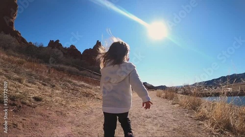Young Caucasian girl happily running along mountain trail on sunny day. Location Colorado.