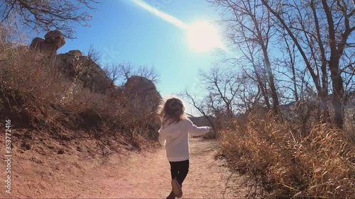 Young Caucasian girl happily running along mountain trail on sunny day. Location Colorado.