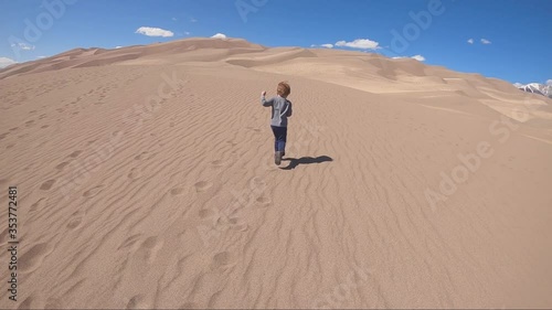 Young Caucasian boy running on beautiful sand dunes in National Park. Location Colorado.