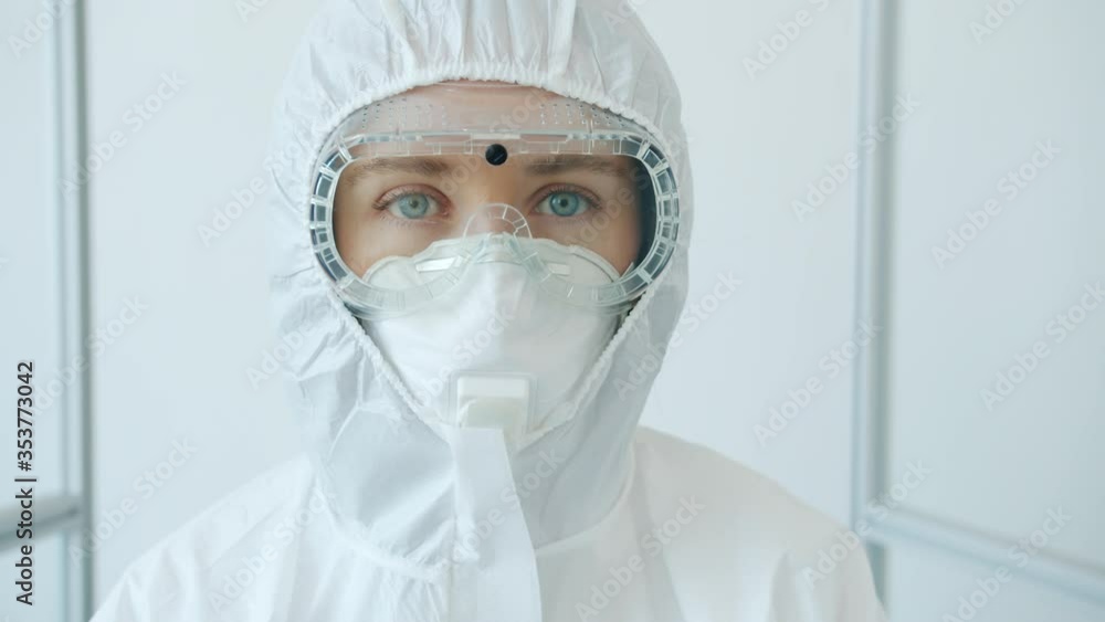 Portrait of young woman doctor in protective goggles, respirator and suit standing in clinic alone and looking at camera. Medicine, quarantine and people concept. Portrait of young woman doctor in protective goggles, respirator and suit standing in clinic alone and looking at camera. Medicine, quarantine and people concept.