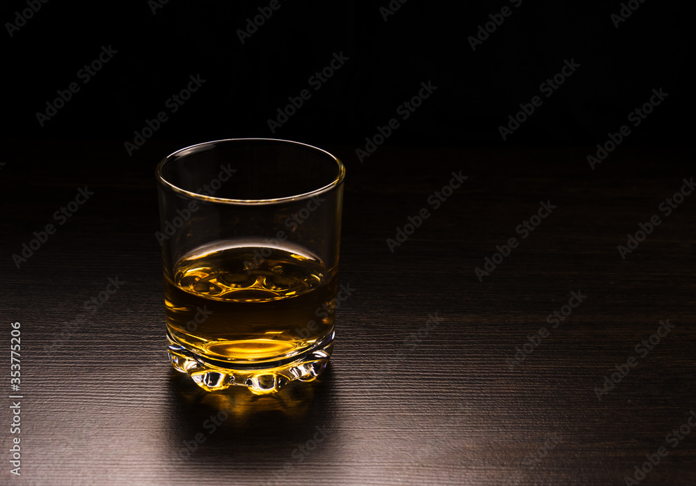 A glass with a whiskey table made of dark wood on a dark background. A glass with a whiskey table made of dark wood on a dark background.