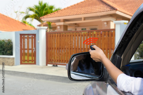 Woman in car, hand using remote control to open the automatic gate with modern home background..The auto gate and security system. photo