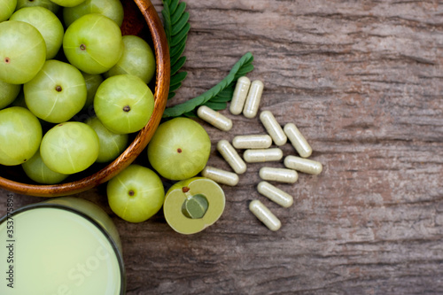 Close-up fresh organic green Amla or Indian gooseberry fruits ( phyllanthus emblica ) with capsules and glass of gooseberry juice tea isolated on rustic wood table background. Overhead view. Flat lay. photo