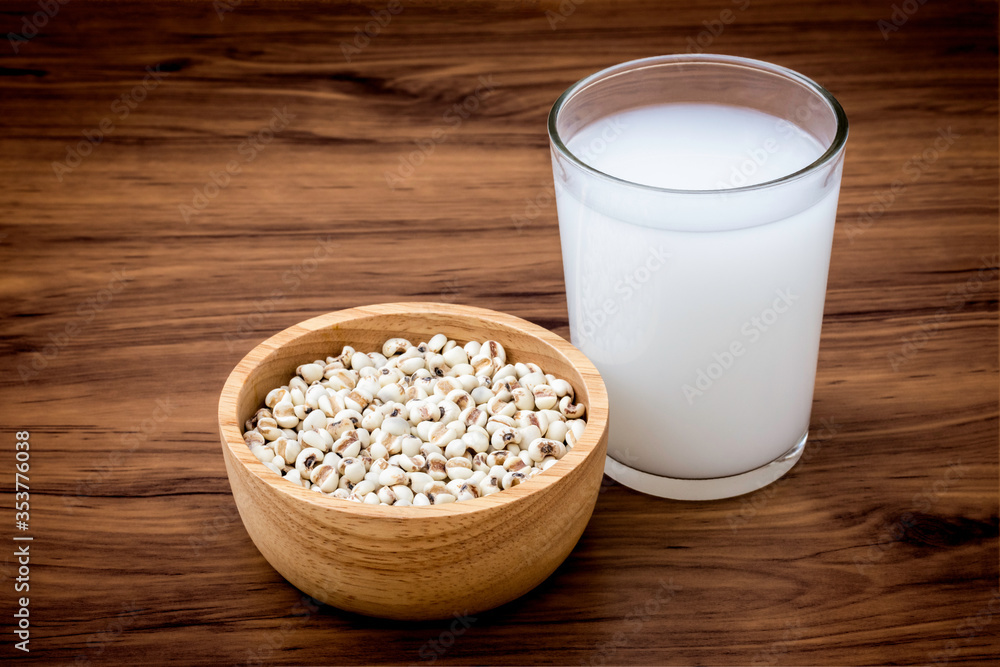 Closeup white Job's tears ( Adlay millet or pearl millet ) in wooden bowl and glass of fresh millet milk isolated on wood table background. Closeup white Job's tears ( Adlay millet or pearl millet ) in wooden bowl and glass of fresh millet milk isolated on wood table background.