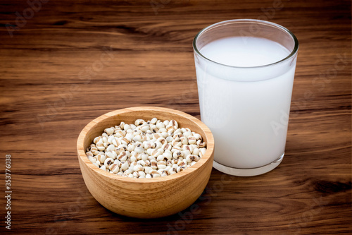 Closeup white Job's tears ( Adlay millet or pearl millet ) in wooden bowl and glass of fresh millet milk isolated on wood table background. 