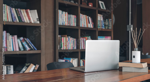 Laptop computer on wooden table in contemporary room with book shelf background. Copy space.
