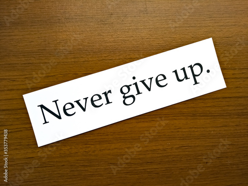 The sentence "Never give up." in white paper on wooden pattern background.