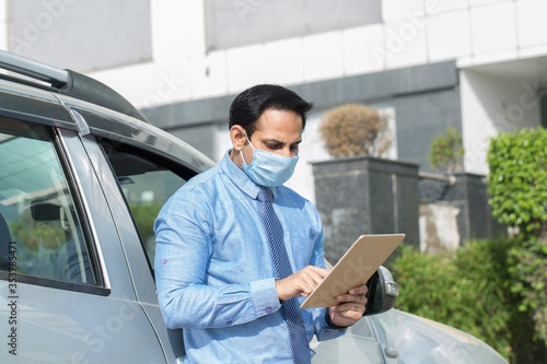 Businessman wearing face mask using his tablet computer outdoors as a mobile office in isolation © G-images