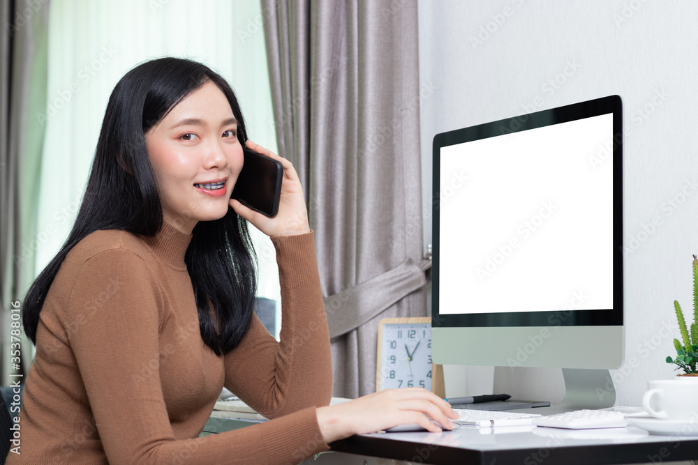 Smiling business asian woman freelancer working remotely from home. Her is speaking on the phone looking at the camera. Stay at home mom working remotely on computer. Smiling business asian woman freelancer working remotely from home. Her is speaking on the phone looking at the camera. Stay at home mom working remotely on computer.