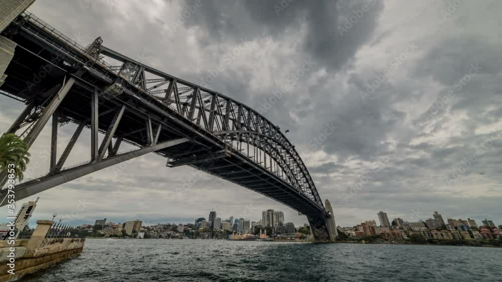 Time lapse looking under the famous Sydney Harbour Bridge with storm clouds in the sky above and city buildings on the horizon in the background. Time lapse looking under the famous Sydney Harbour Bridge with storm clouds in the sky above and city buildings on the horizon in the background.