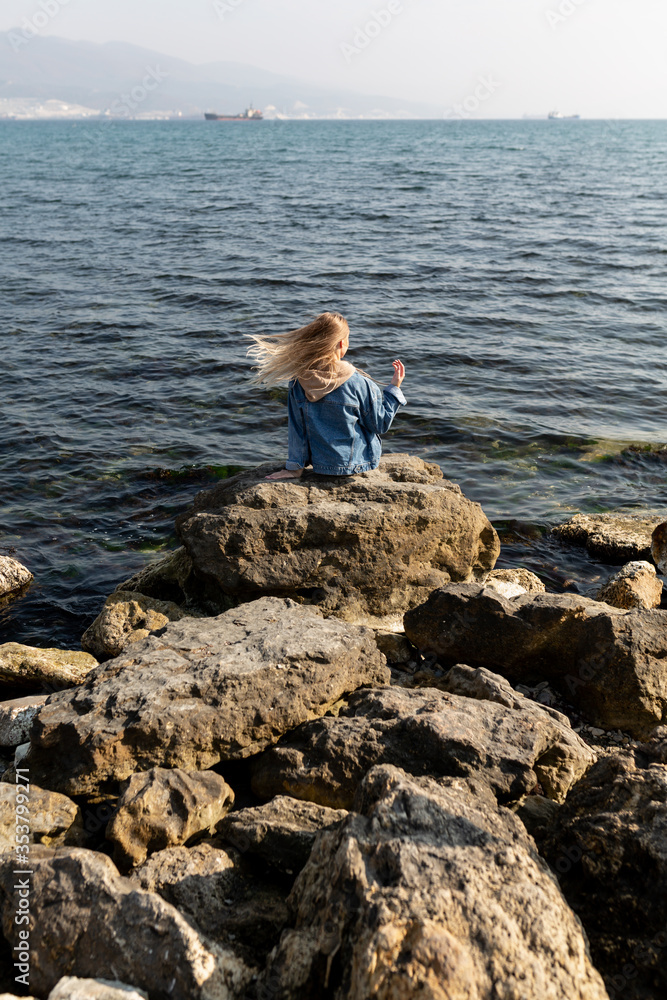 Beautiful woman with developing hair in the wind on the stones on the seashore against the backdrop of the port and ships. Beautiful vacation and travel photos. Happy weekend. Beautiful woman with developing hair in the wind on the stones on the seashore against the backdrop of the port and ships. Beautiful vacation and travel photos. Happy weekend.