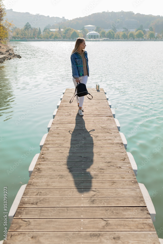 Beautiful woman walking on a pier on a lake on a background of rolling hills. Great photos from vacation and travel. Happy holiday.