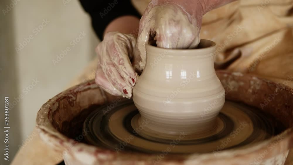 Female potter's hands with red manicure working with wet clay on a pottery wheel making a clay product in a workshop. Unrecognizable female person forming a vase, pulls it up Female potter's hands with red manicure working with wet clay on a pottery wheel making a clay product in a workshop. Unrecognizable female person forming a vase, pulls it up