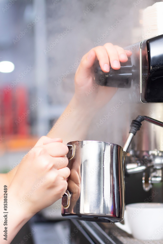 Coffee shop worker preparing coffee on steam espresso coffee machine. Barista Warming Milk In Metal Jug With Steam Of Coffee Machine. vertical photo