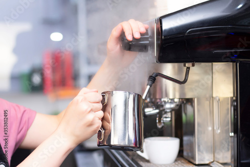 Coffee shop worker preparing coffee on steam espresso coffee machine. Barista Warming Milk In Metal Jug With Steam Of Coffee Machine