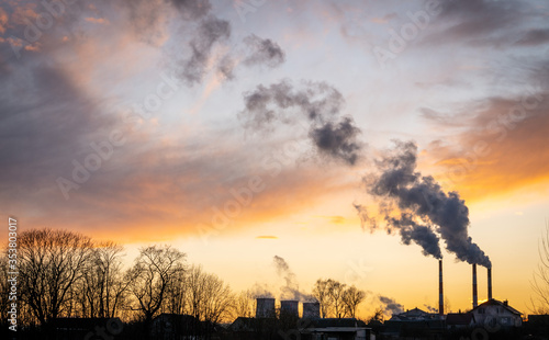 Smoke from the chimneys of a thermal power plant at sunset over plant silhouettes moves from right to left 
