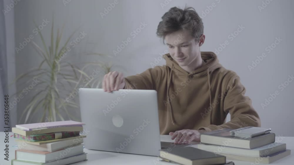 Joyful Caucasian boy entering room, opening laptop and typing on keyboard. Portrait of confident handsome teenager using social media or surfing Internet. Wireless communication, adolescence. Joyful Caucasian boy entering room, opening laptop and typing on keyboard. Portrait of confident handsome teenager using social media or surfing Internet. Wireless communication, adolescence.