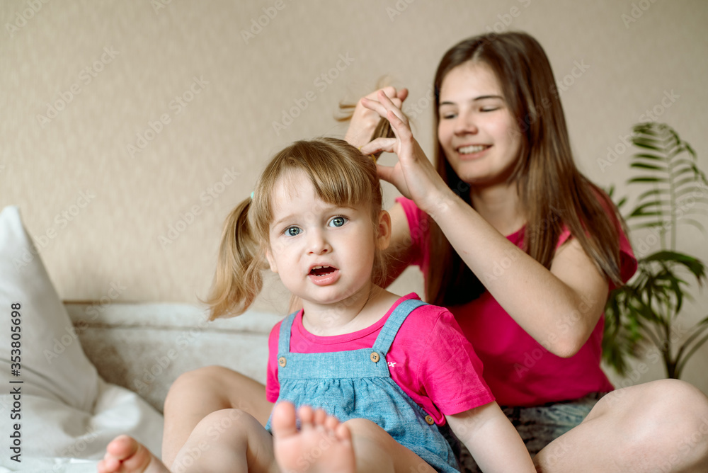 cute sister teen combing hair baby in bed.Cute girls are laughing and smiling. Morning treatments, hair care, care. Family love. Cozy bright bedroom. cute sister teen combing hair baby in bed.Cute girls are laughing and smiling. Morning treatments, hair care, care. Family love. Cozy bright bedroom.