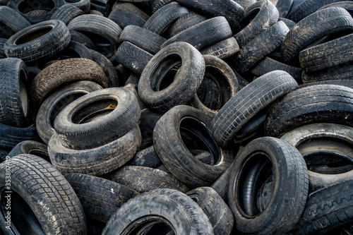 Big pile of automobile tires on the broken-down plant. Many black rubber tyres on the ground inside the old huge empty building.