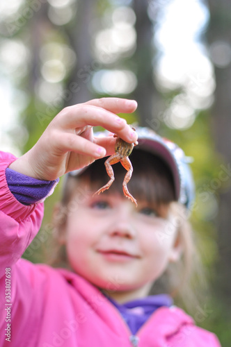 child playing with a frog in the forest, a girl holds a big frog in her hands, a naturalist