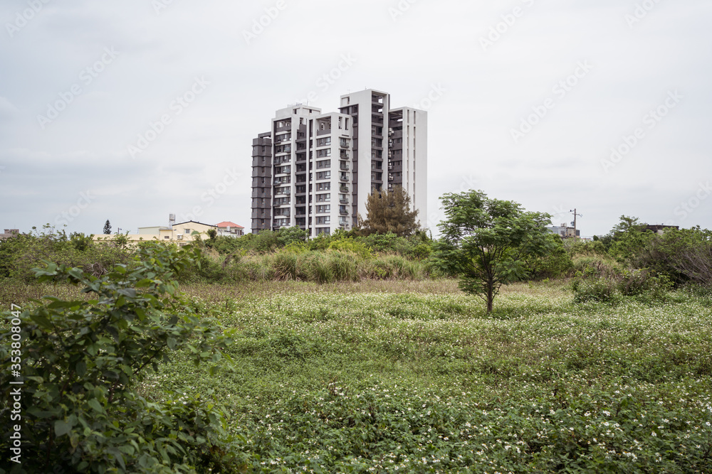 lonely tall apartment building in the middle of green field with tree