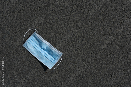 Used medical mask on asphalt. Disposable Face Mask on pavement with copy space. Used Surgical masks haphazardly strewn. Improperly discarding used face mask. 