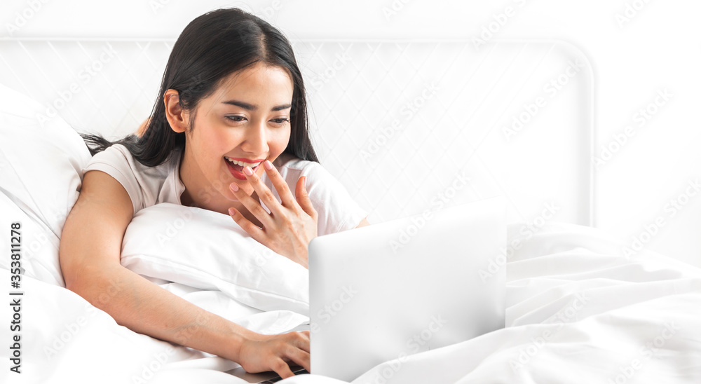 Young asian woman relaxing using laptop computer on bed in the bedroom at home.Young beauty girl working and typing on keyboard at home.work from home concept Young asian woman relaxing using laptop computer on bed in the bedroom at home.Young beauty girl working and typing on keyboard at home.work from home concept