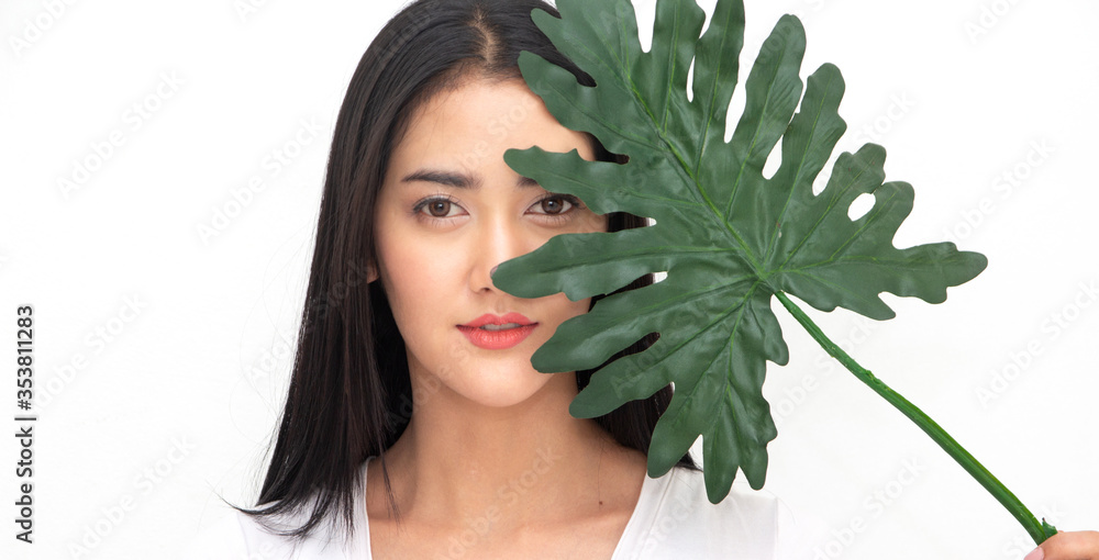 Portrait of smiling happy cheerful beautiful pretty asian woman behind green leaf.skin care and organic cosmetics concept Portrait of smiling happy cheerful beautiful pretty asian woman behind green leaf.skin care and organic cosmetics concept