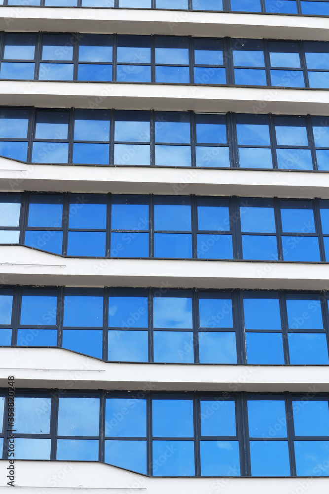 The blue sky is reflected in the windows of a multi-story office building. Abstract city background. The blue sky is reflected in the windows of a multi-story office building. Abstract city background.