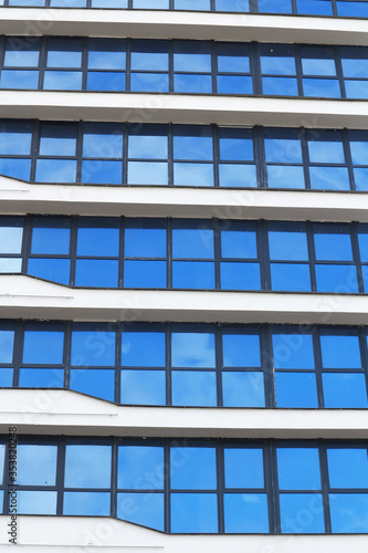 The blue sky is reflected in the windows of a multi-story office building. Abstract city background.