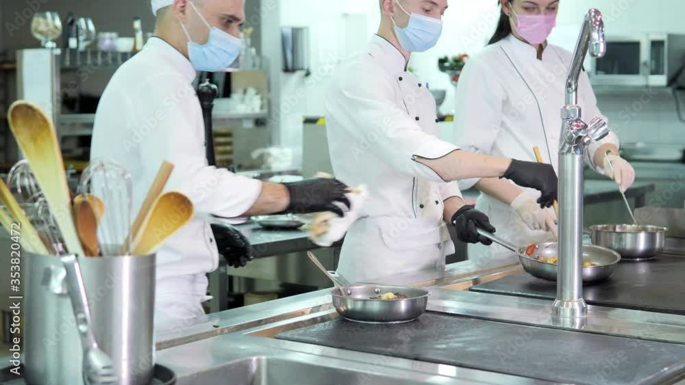 Chefs in protective masks and gloves prepare food in the kitchen of a restaurant or hotel Chefs in protective masks and gloves prepare food in the kitchen of a restaurant or hotel