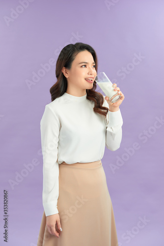 Portrait of a satisfied young asian woman drinking milk from the glass isolated over purple background