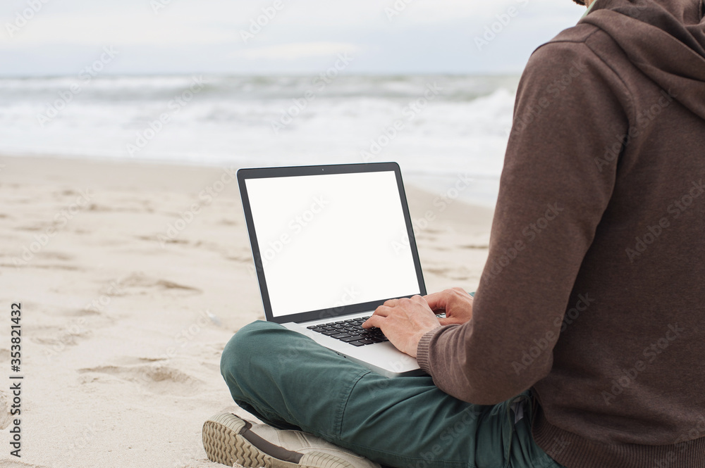 Young man using laptop computer on a beach, white blank, empty screen monitor, Freelance work, technology, distance education, studying, vacations, travel concept