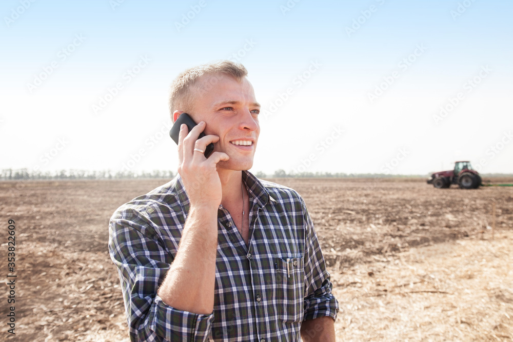 Young attractive man with telephone near a tractor. Concept of agriculture and field works. Young attractive man with telephone near a tractor. Concept of agriculture and field works.