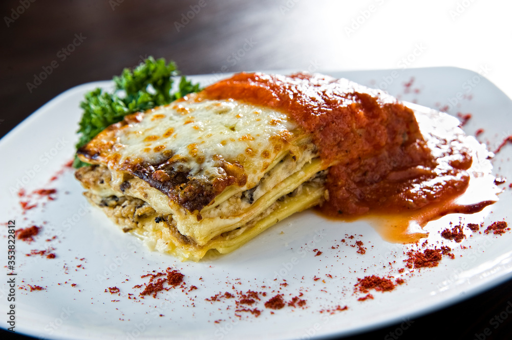 Golden lasagne with meat, tomatoes, cheese sauce and pasta in alternating layers on a wooden board garnished with basil Golden lasagne with meat, tomatoes, cheese sauce and pasta in alternating layers on a wooden board garnished with basil