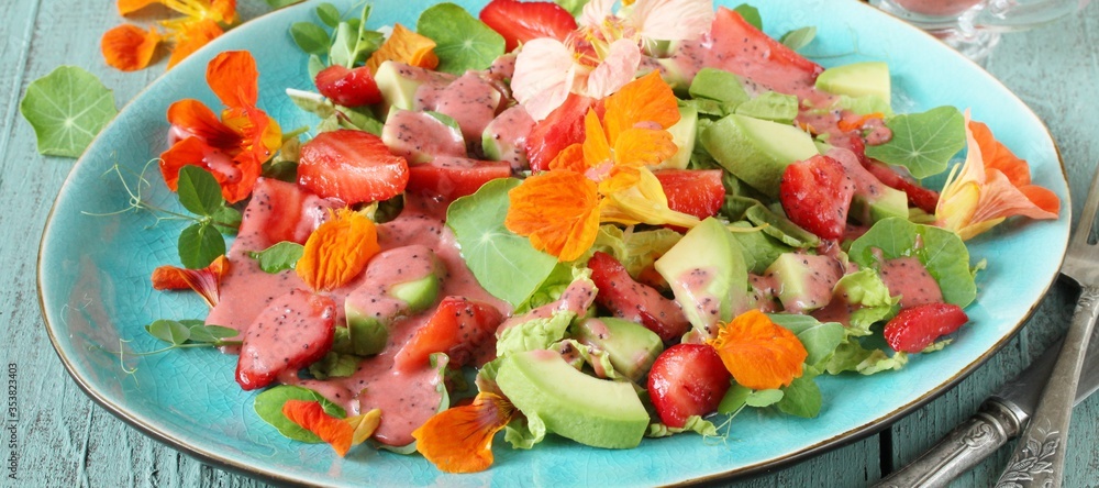 salad with nasturtium flowers and leaves with strawberries and avocados. dressed with strawberry vinaigrette or strawberry dressing with poppy seeds.