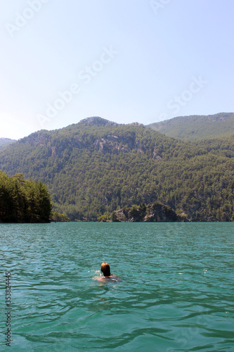 Young woman swims in a lake among the mountains. Summer mood.