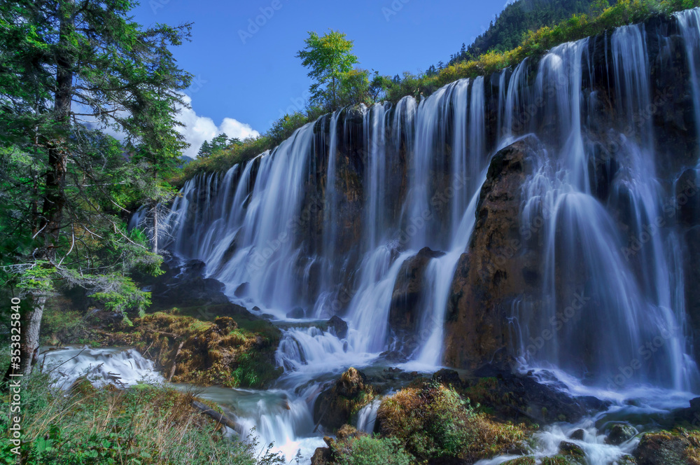 Beautiful and fresh scenery at waterfalls with massive cascade, green algae, reflection and trees.