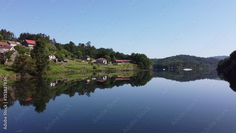 Aerial Drone above river lake at Fornelos de Montes, Spain. Dolly approach shot at beautiful calm nature scene with reflected water with dense forested hills. Homes or resort in Galicia high at alpine Aerial Drone above river lake at Fornelos de Montes, Spain. Dolly approach shot at beautiful calm nature scene with reflected water with dense forested hills. Homes or resort in Galicia high at alpine