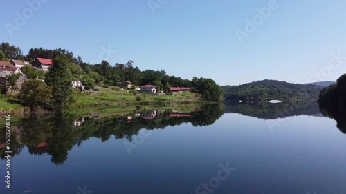 Aerial Drone above river lake at Fornelos de Montes, Spain. Dolly approach shot at beautiful calm nature scene with reflected water with dense forested hills. Homes or resort in Galicia high at alpine photo