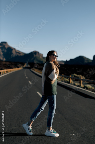 a young girl with long hair in hipster clothes and sunglasses walks on an empty asphalt road © Richard