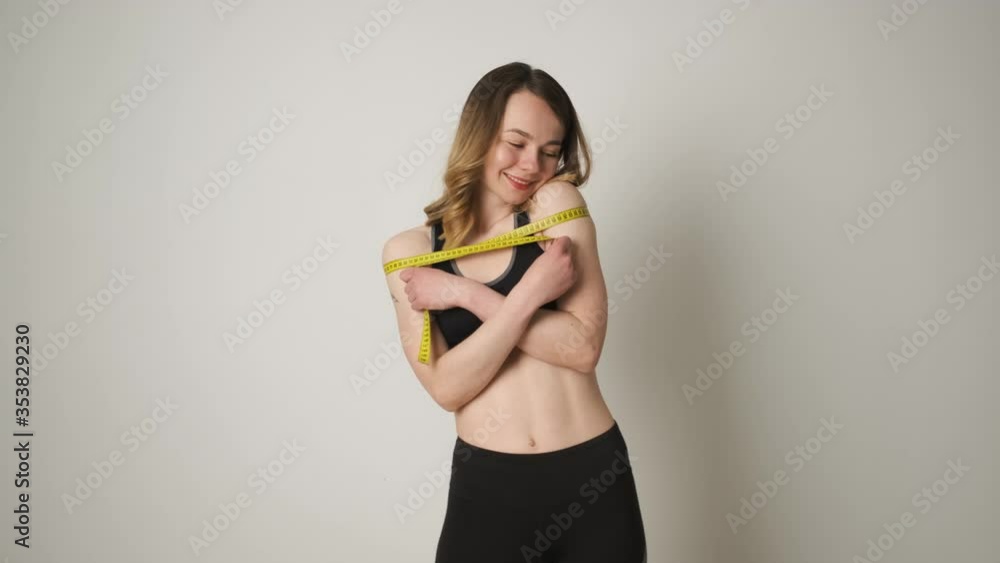 Portrait of a slender girl in sportswear who measures the body with a tape measure after exercise and happy with the result Portrait of a slender girl in sportswear who measures the body with a tape measure after exercise and happy with the result