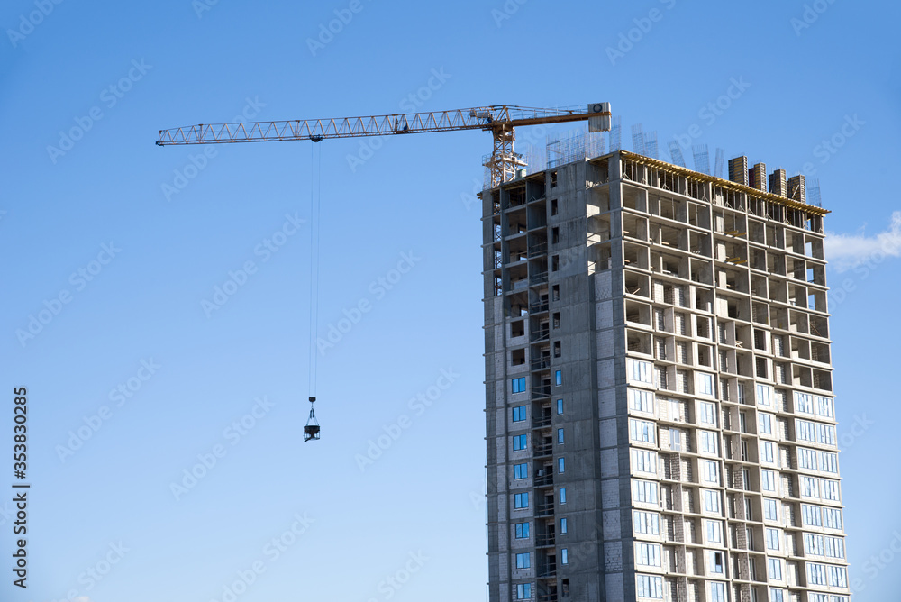 Tower crane lifting concrete bucket for pouring concrete during construction new residential building on blue sky background. Builder workers during formworks and pouring concrete