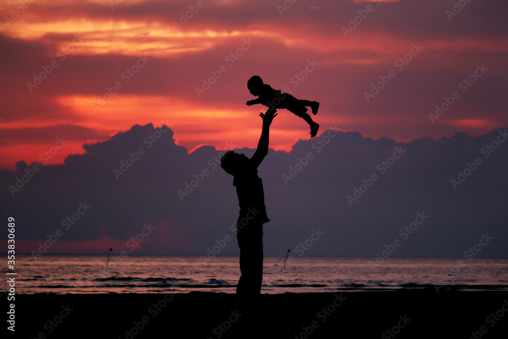 Father and little daughter play silhouettes on beach at sunset