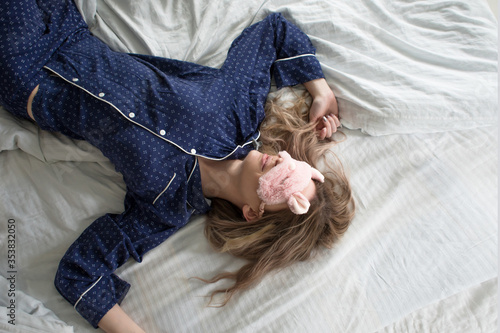 Cute blonde in her bed in blue pajamas and sleep mask,