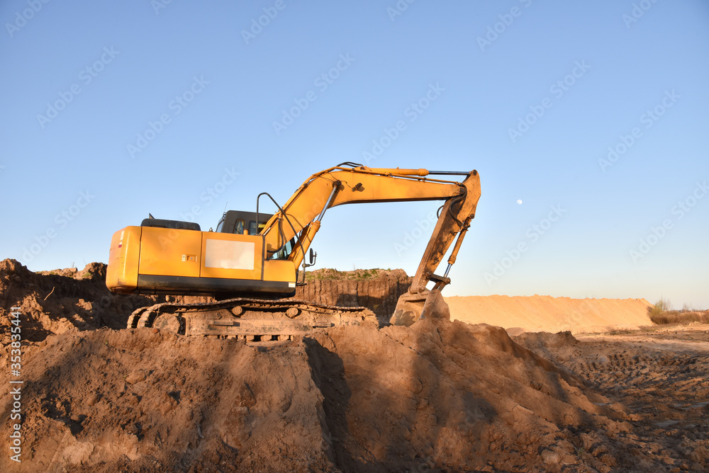 Excavator working on earthmoving. Backhoe digs ground in sand quarry on blue sky background. Construction machinery for excavation, loading, lifting and hauling of cargo on job sites Excavator working on earthmoving. Backhoe digs ground in sand quarry on blue sky background. Construction machinery for excavation, loading, lifting and hauling of cargo on job sites