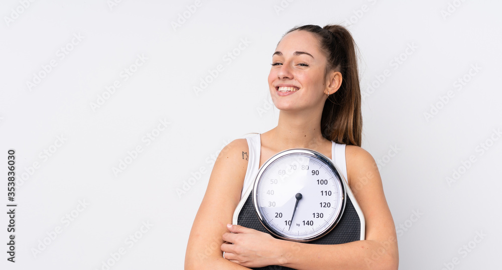Young brunette woman over isolated white background with weighing machine Young brunette woman over isolated white background with weighing machine