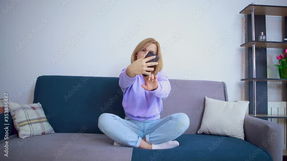 Beautiful blonde girl takes a selfie while sitting on a sofa. Beautiful blonde girl takes a selfie while sitting on a sofa.