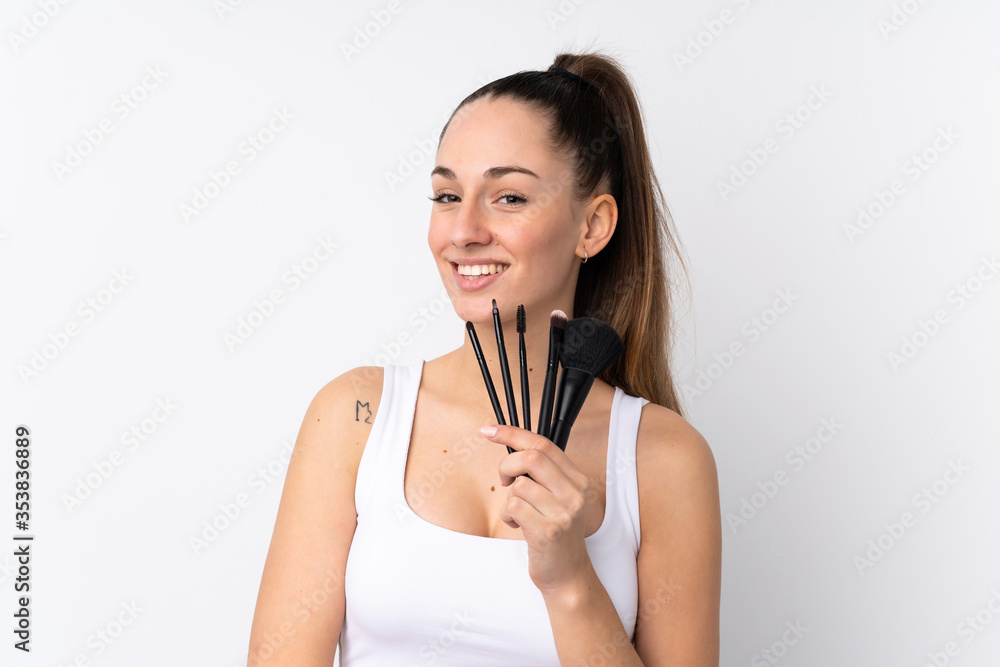 Naklejka premium Young brunette woman over isolated white background holding makeup brush