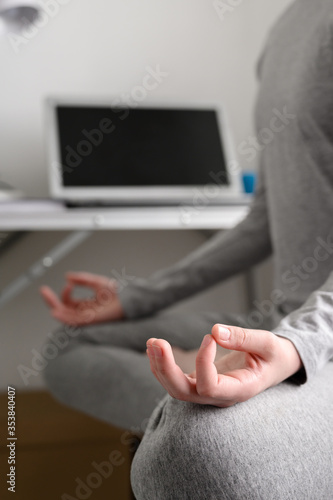 Teen girl is training at home  doing yoga exercises  sitting in lotus position  meditation. Body close-up  focus on the hand. Remote workout at home.